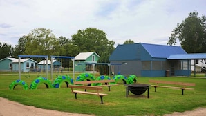 Un parque infantil con columpios de neumáticos verdes y azules, mesas de picnic y un edificio con techo azul.