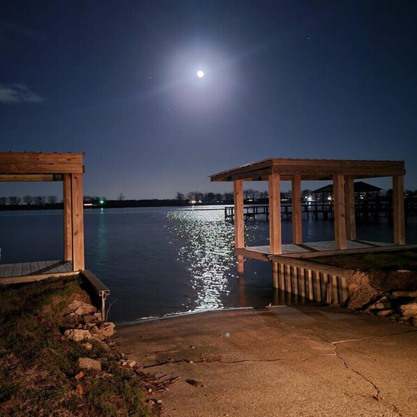 A wooden dock extending into a calm lake at night with a full moon in the sky.