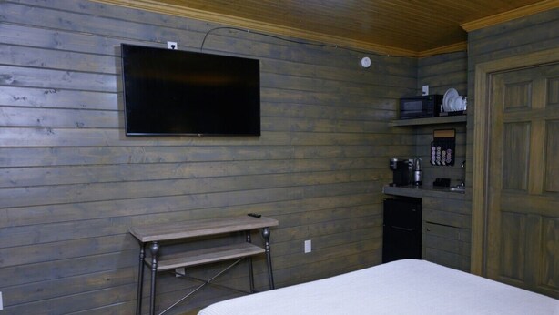 A room with a bed, a television mounted on the wall, a small table, and a kitchenette area with a microwave and coffee maker. - Peaceful Orchard Getaway! High-Speed Internet! (Lake Village)