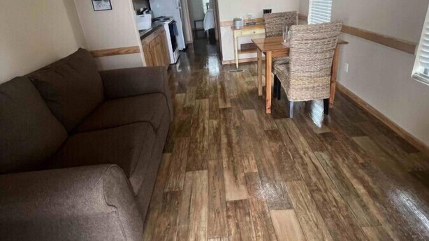 Een woonkamer met een bruine bank, een eethoek met een tafel en stoelen, en een keuken op de achtergrond.