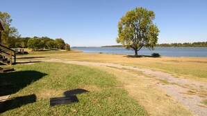 Une zone herbeuse avec un arbre et une vue dégagée sur un lac.