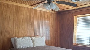 Een slaapkamer met een bed, houten wanden, een plafondventilator en een raam met zonwering.