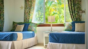 A room with two beds, a nightstand, a lamp, and a window with curtains.
