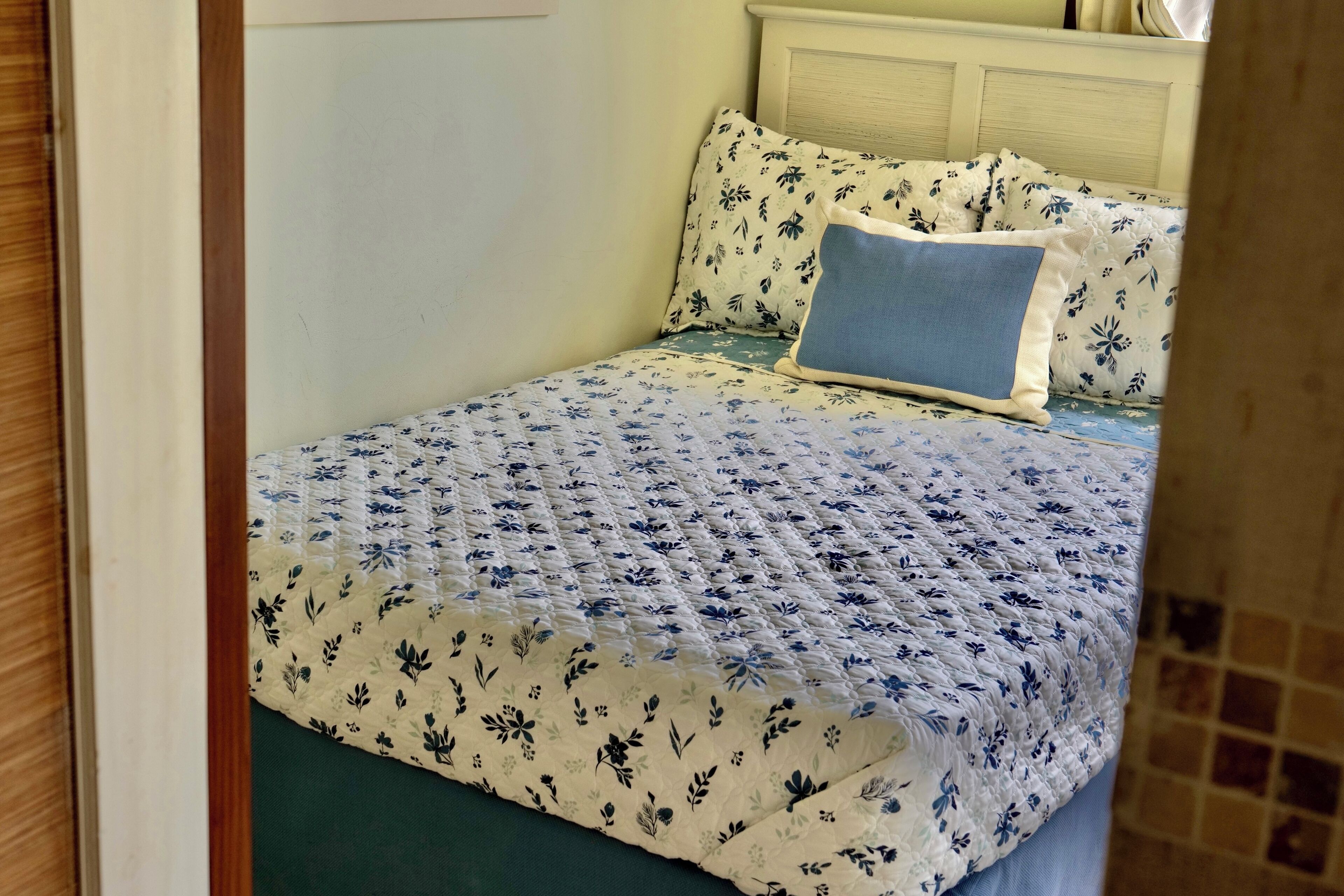 A neatly made bed with floral bedding, a blue pillow, and a wooden headboard.
