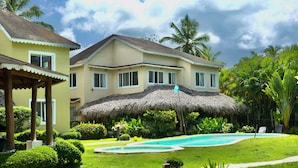 A resort with a swimming pool, a thatched-roof structure, and lush greenery.