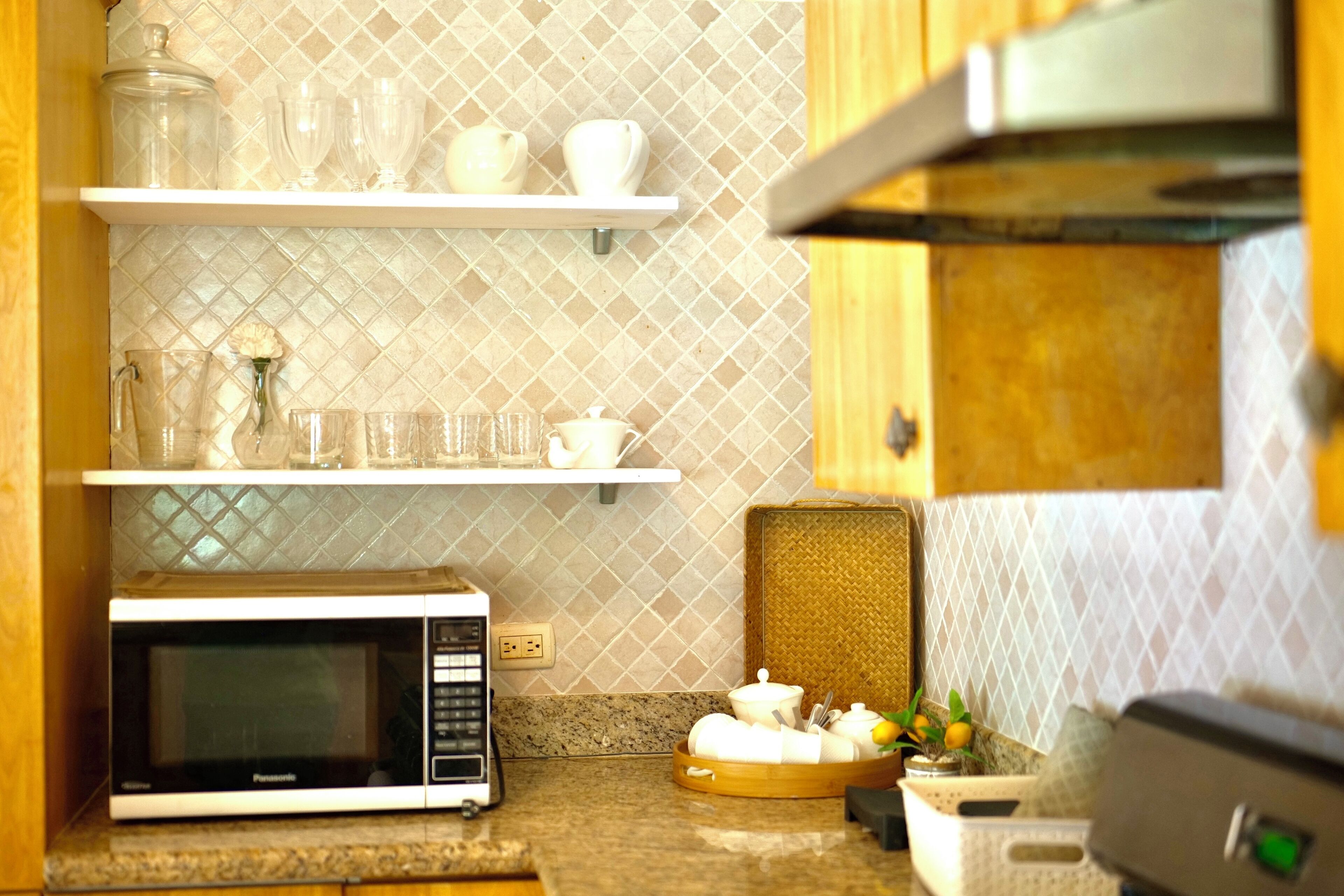A kitchen with a microwave, shelves with glassware, and a fruit bowl.