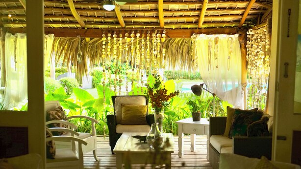A room with a wooden ceiling, white furniture, and a view of lush greenery.