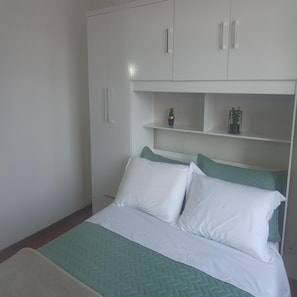 A bedroom with a bed, white and green bedding, a green herringbone-patterned bedspread, and white cabinets with handles. - Apartamento Funcional em Curitiba (Curitiba)