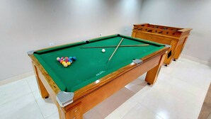 Una mesa de billar con bolas y tacos, una mesa de futbolín de madera y un suelo de baldosas.