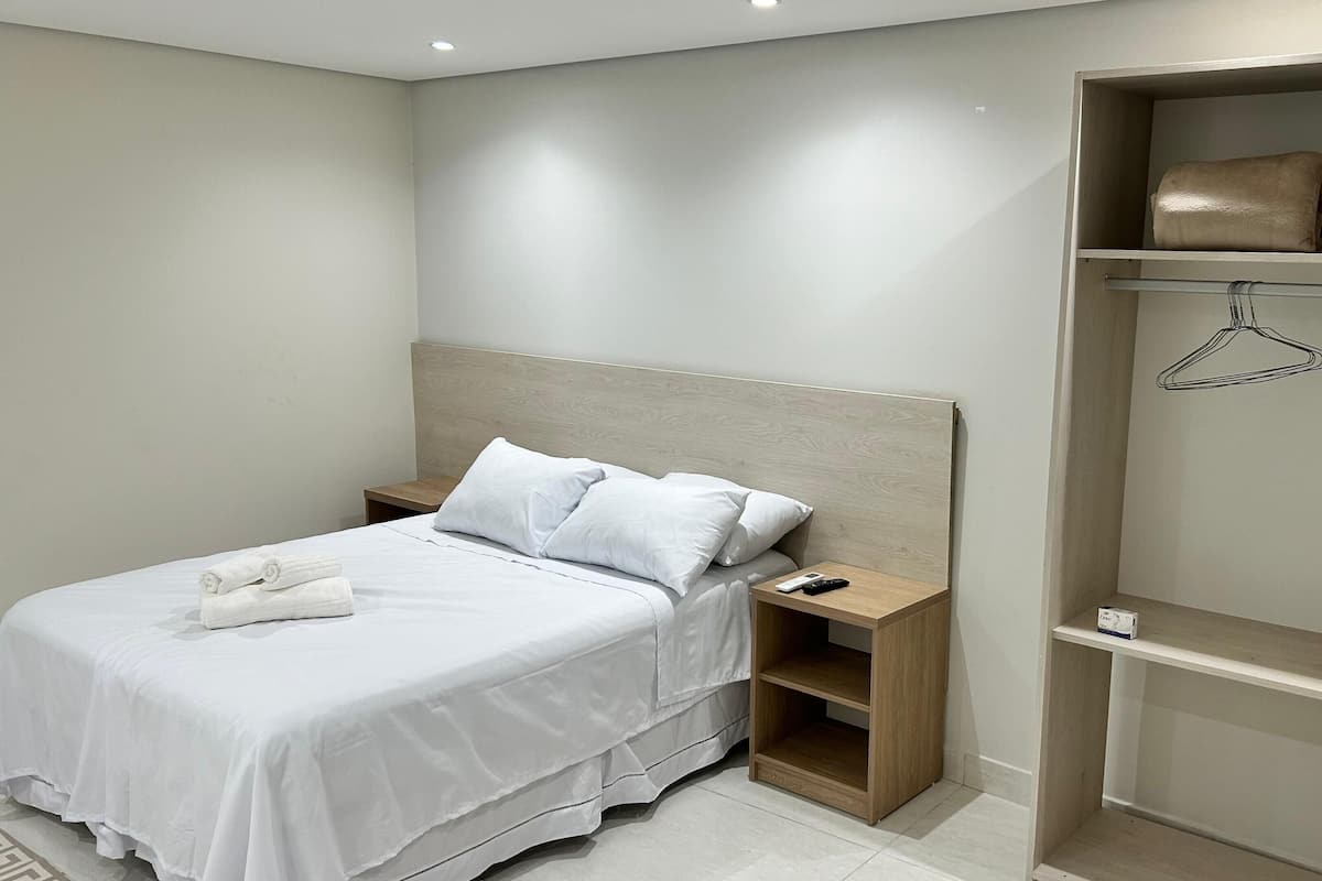 Ein Schlafzimmer mit Bett, Nachttischen, einem Kleiderschrank und einer Kleiderstange.