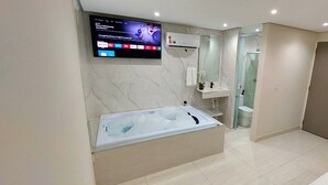 Un baño moderno con una bañera grande, un televisor montado en la pared y un área de ducha independiente.