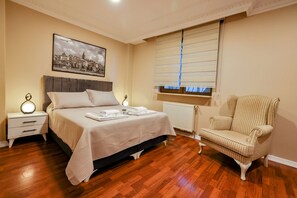 Une chambre à coucher avec un lit, des tables de chevet, une chaise, une fenêtre avec des stores et un tableau représentant un paysage urbain accroché au mur.