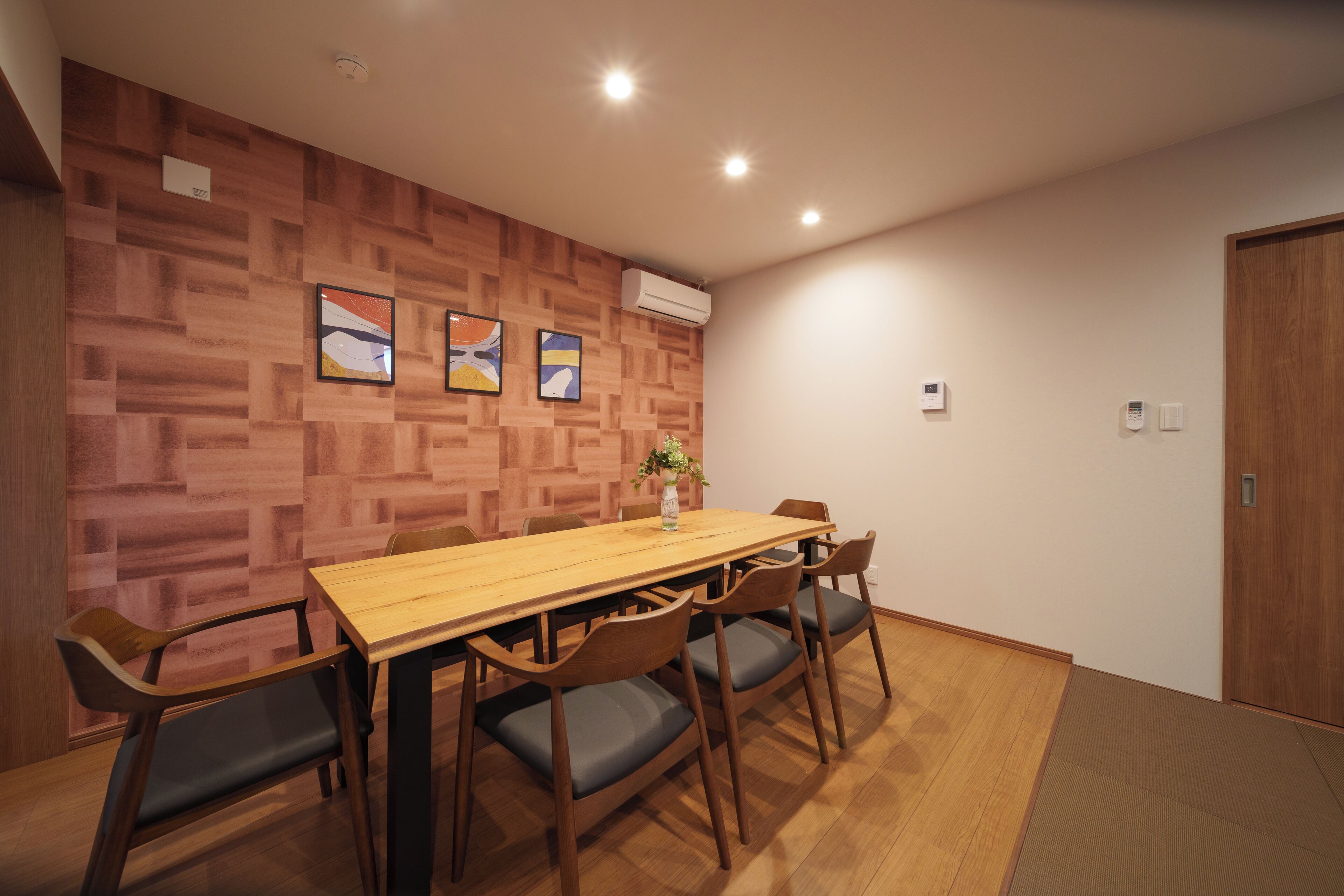 A conference room with a wooden table and chairs, a plant on the table, and a wooden wall with framed pictures.