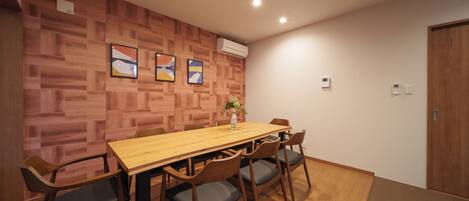 Une salle de conférence avec une table et des chaises en bois, une plante posée sur la table et un mur en bois orné de tableaux.
