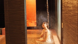 A person sitting in a hot spring area with a wooden floor and a glass partition. - Sanwa sen (Beppu)
