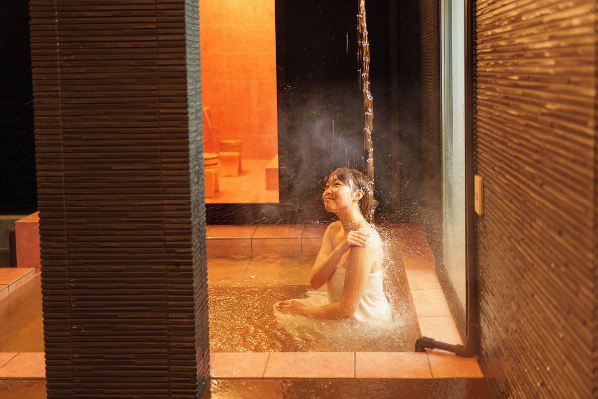 A person sitting in a hot spring area with a wooden floor and a glass partition.