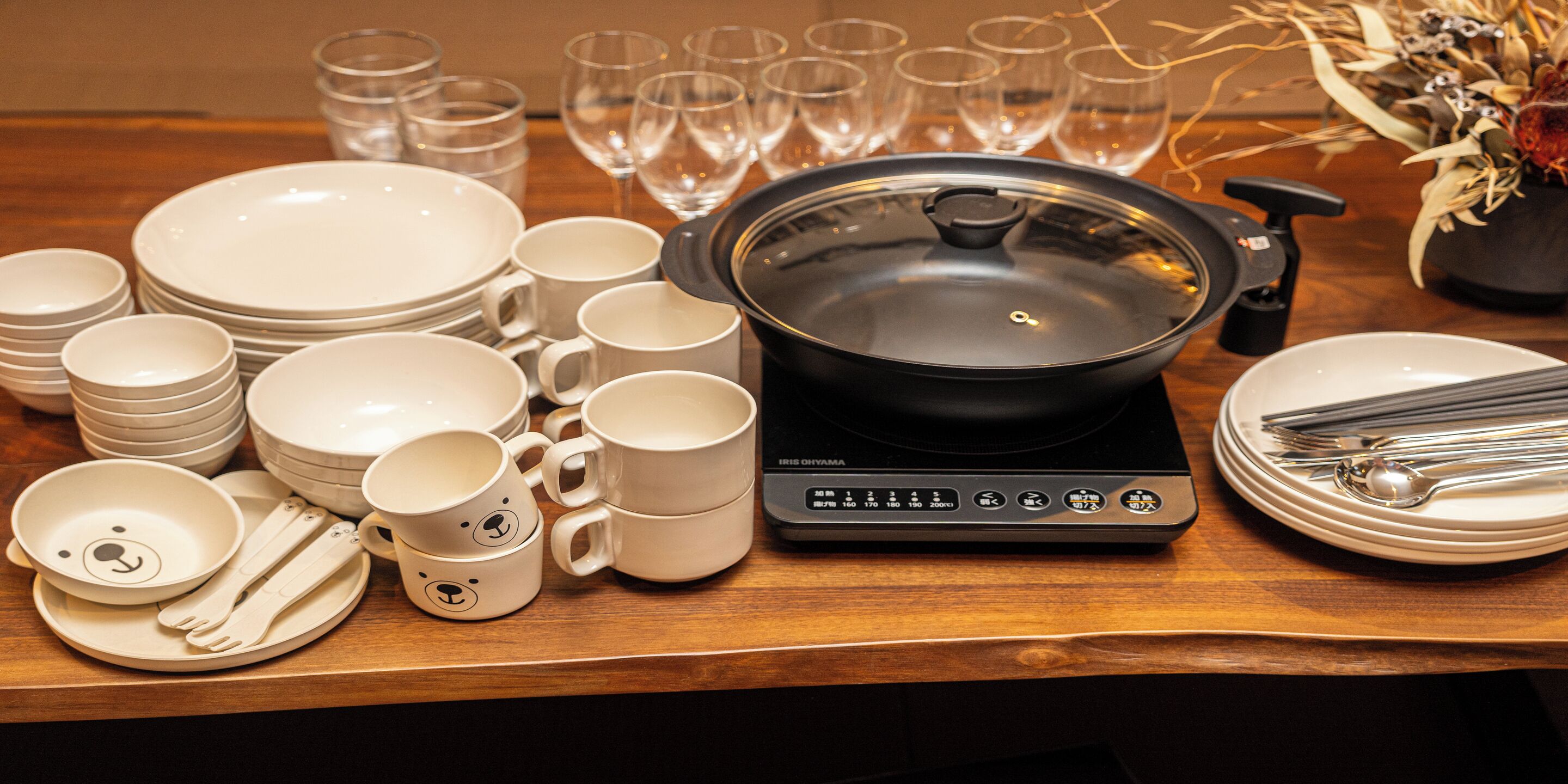 A table set with white plates, bowls, mugs, and cutlery, including a rice cooker and a pot.