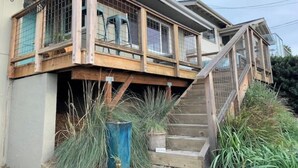 Une maison à deux étages dotée d’une terrasse en bois et d’un escalier menant à l’étage supérieur.