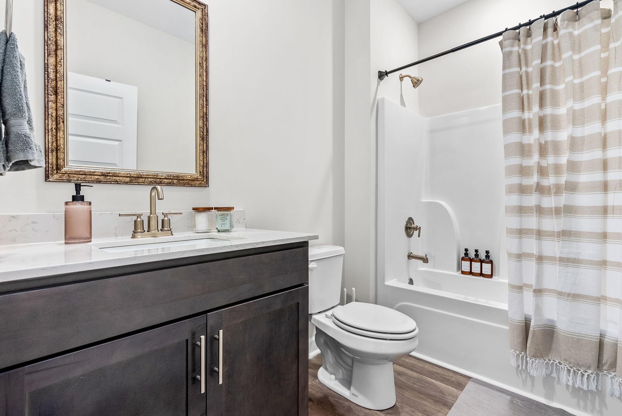 A modern bathroom with a white sink, dark cabinets, a toilet, and a shower area with a striped curtain.
