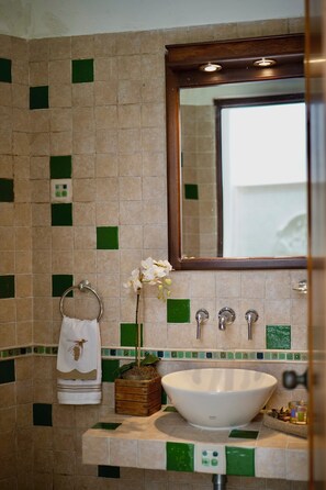 A bathroom with a white sink, green and beige tiles, a wooden box with a plant, and a towel with a bird design.