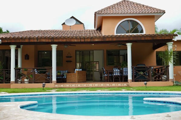 A resort with a swimming pool, covered patio with outdoor furniture, and a large window.