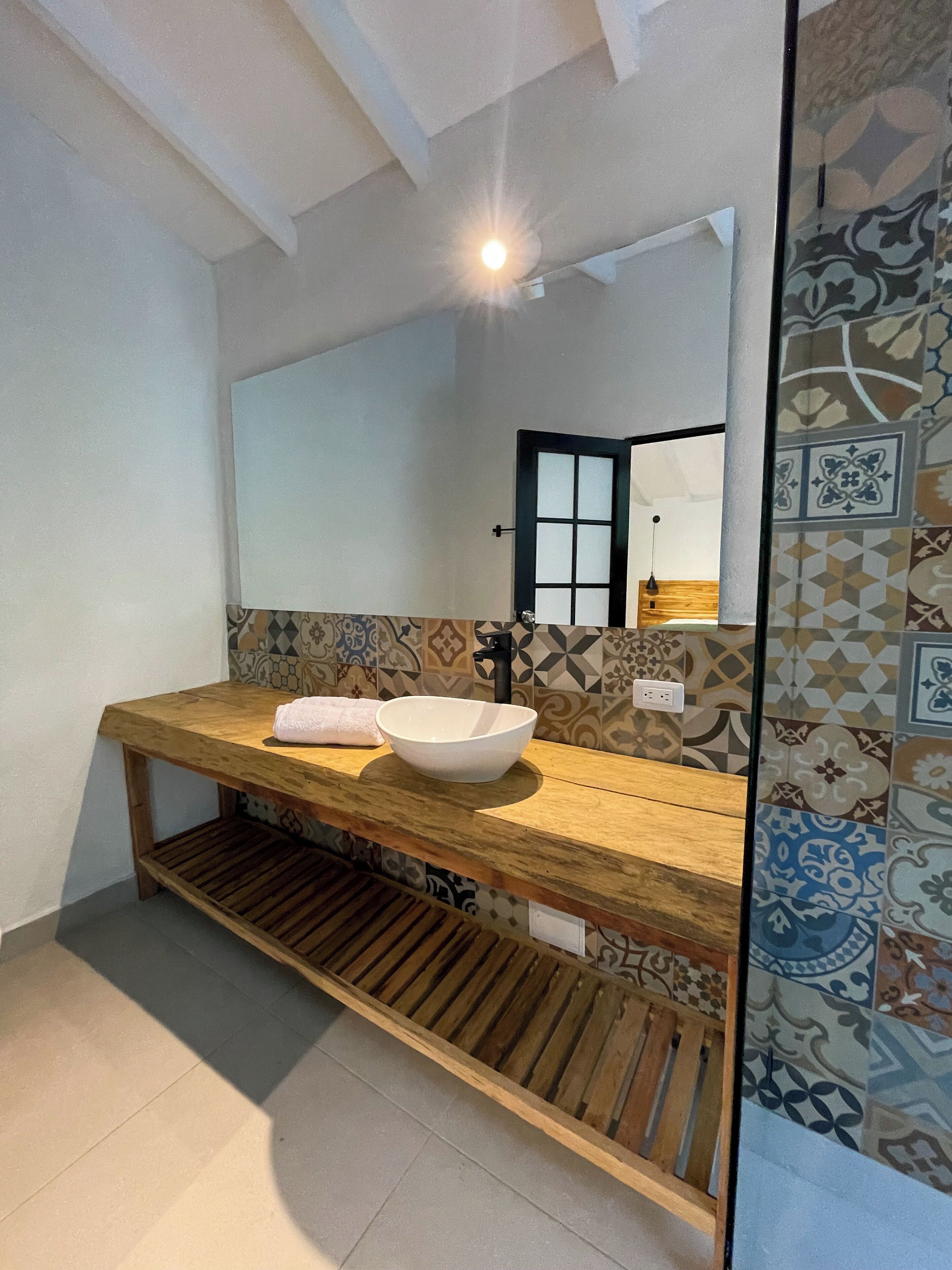 A bathroom with a wooden vanity, a white basin, and patterned tiles.