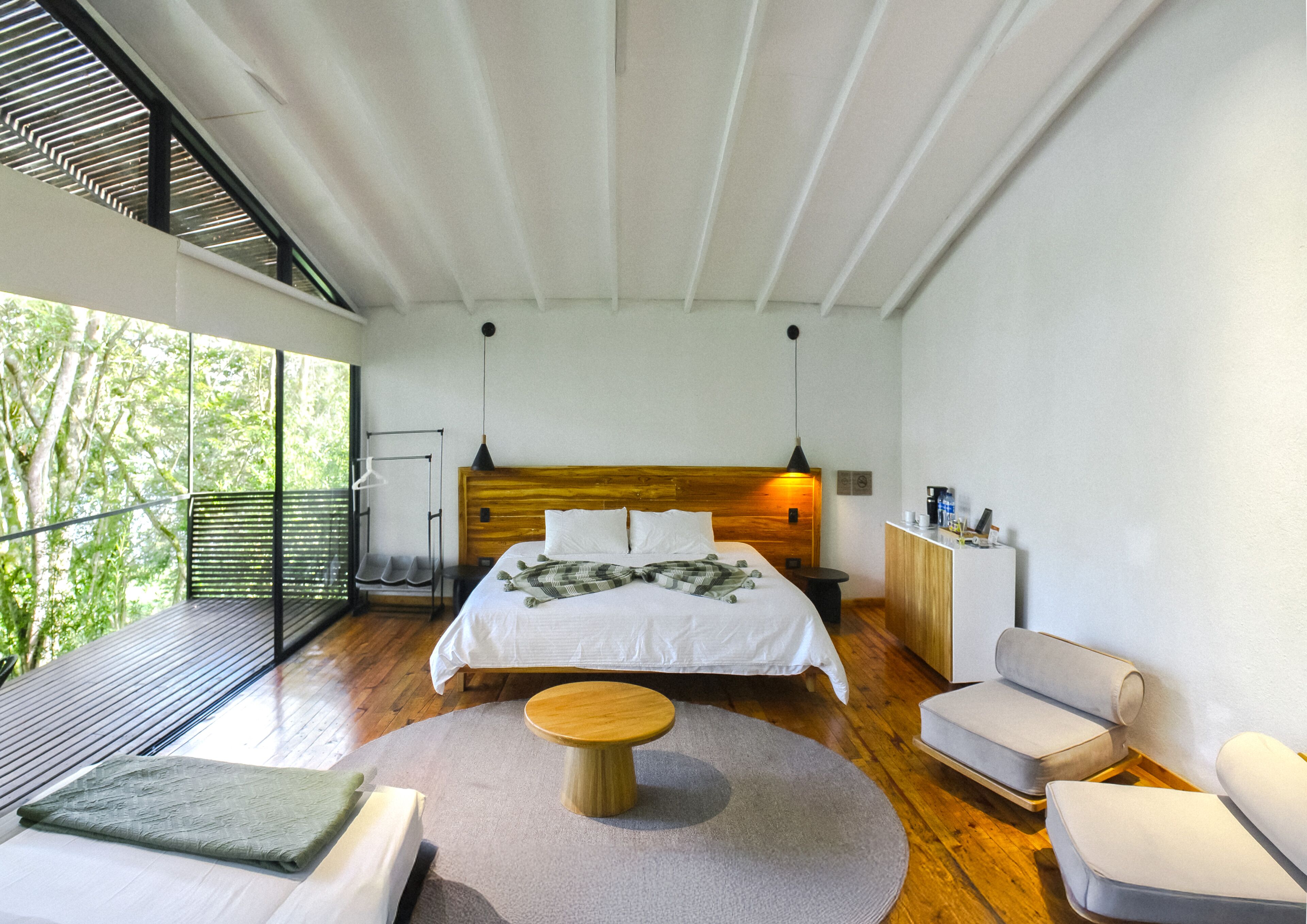 Quarto moderno com uma cama grande, uma mesa redonda de madeira e um espaço de estar com duas cadeiras.