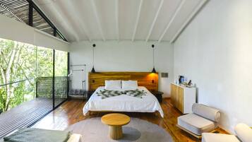Quarto moderno com uma cama grande, uma mesa redonda de madeira e um espaço de estar com duas cadeiras.