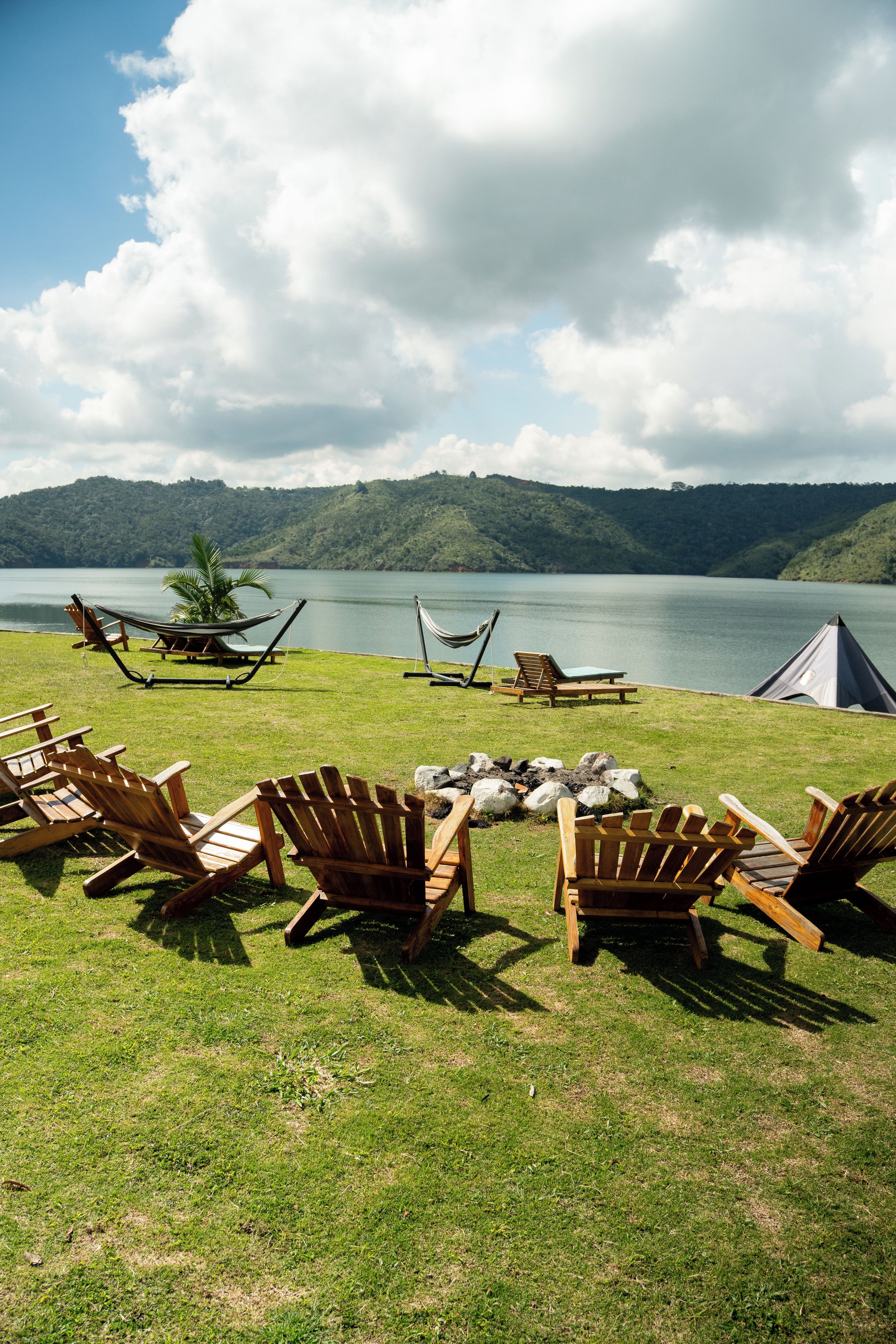 A lakeside campsite with wooden chairs, a hammock, and a tent.