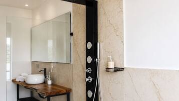 Un bagno moderno con parete in marmo, uno specchio grande, un mobile lavabo in legno, un box doccia nero e un piccolo ripiano con articoli da toilette.