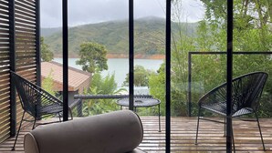 A modern outdoor seating area with a sofa and chairs, overlooking a scenic landscape with hills and a body of water.
