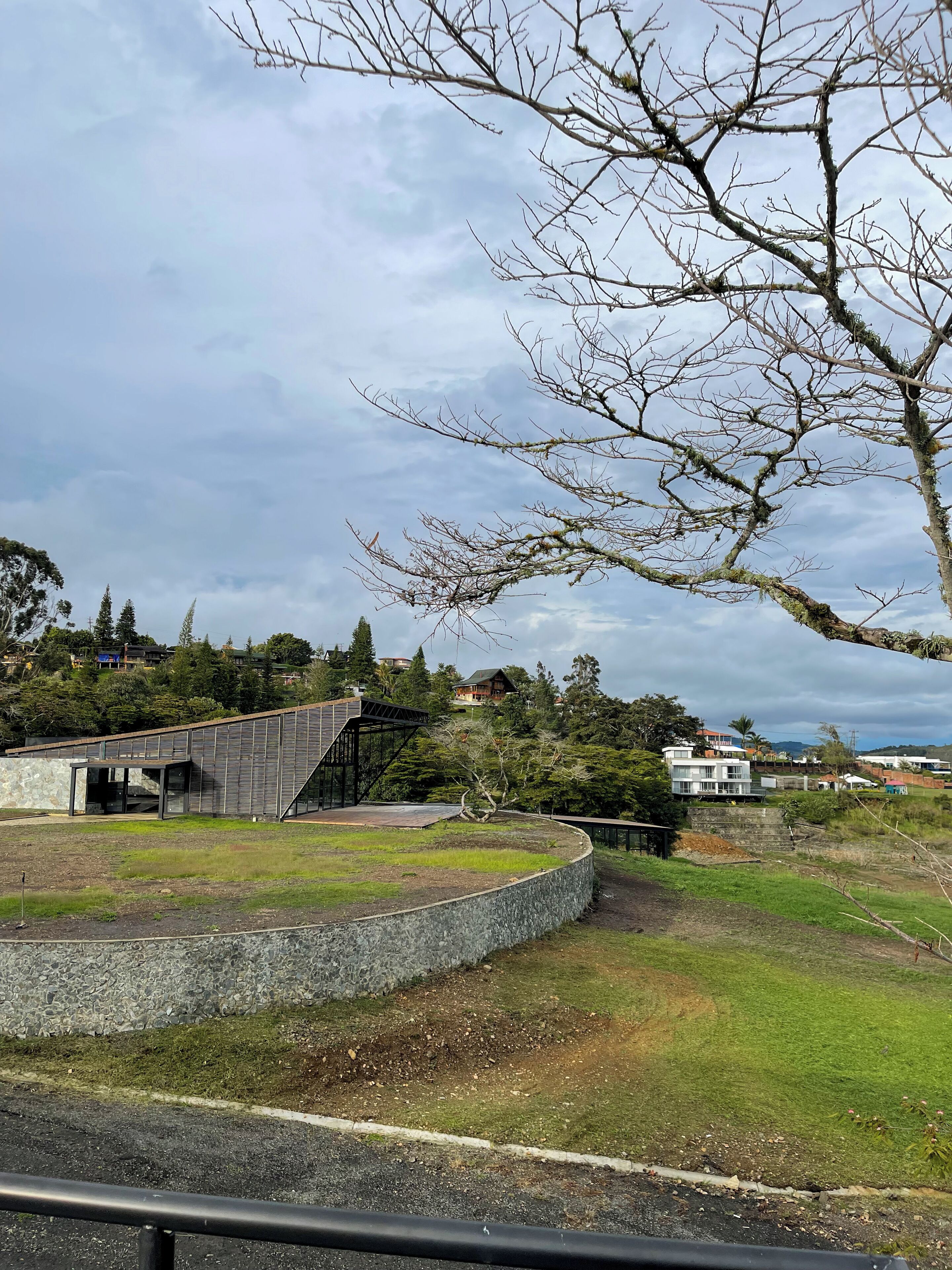 A modern building with a glass facade, a stone retaining wall, and a grassy area in front.