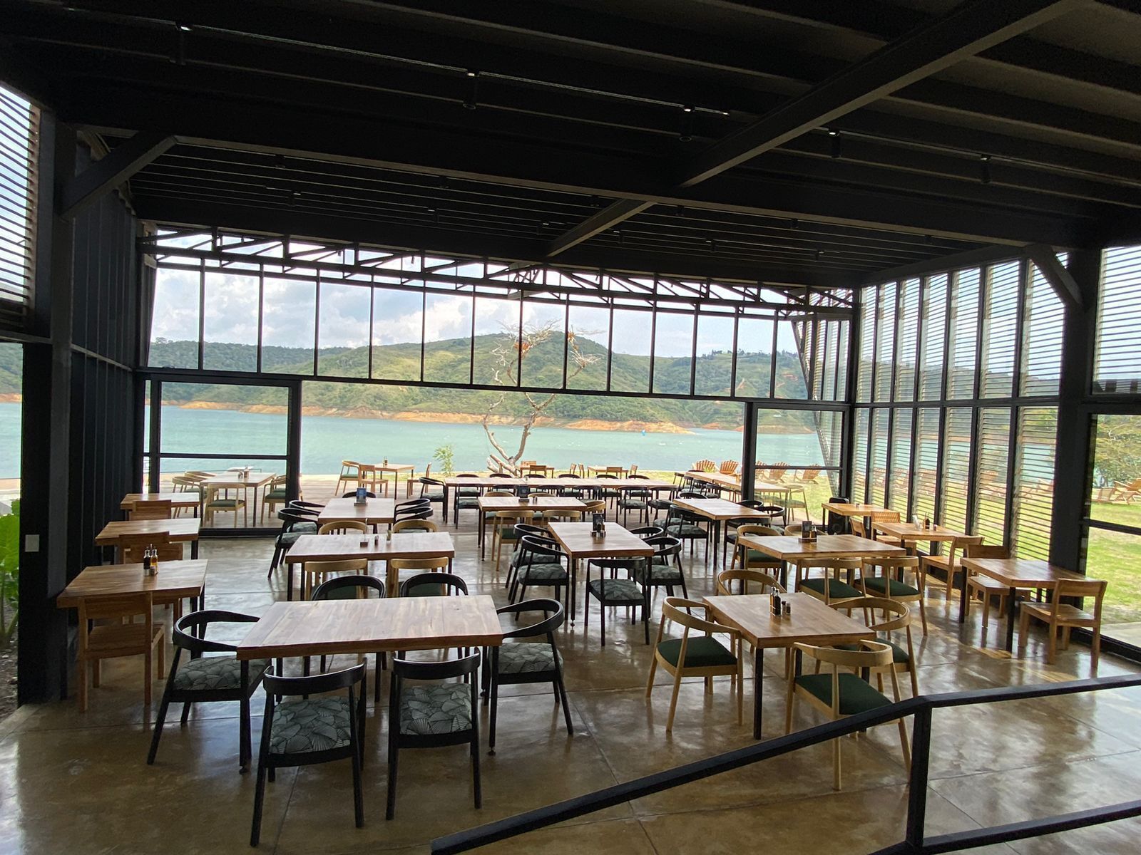 Un espace de restauration intérieur avec des tables et des chaises, de grandes fenêtres offrant une vue sur la mer et les collines.