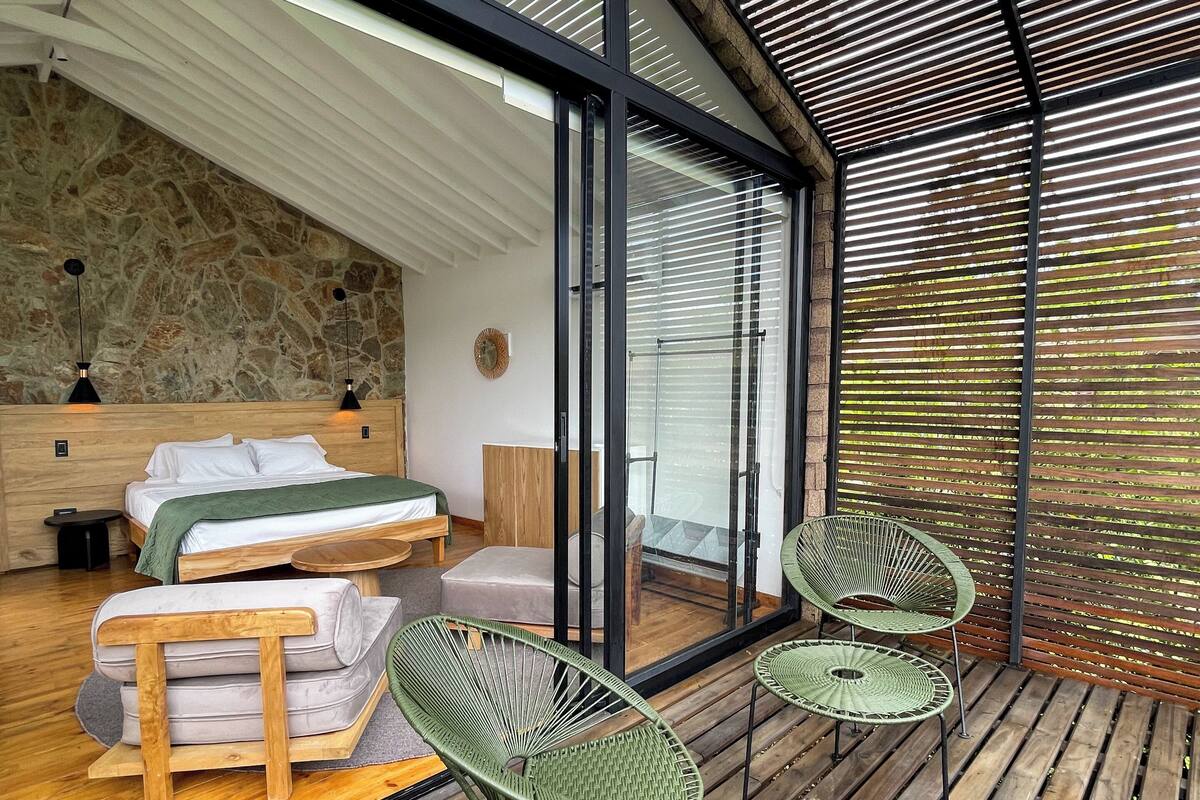 A modern bedroom with a large bed, a wooden bench, and two green chairs.