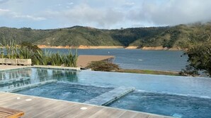 A pool area with wooden loungers and a view of the sea and hills.