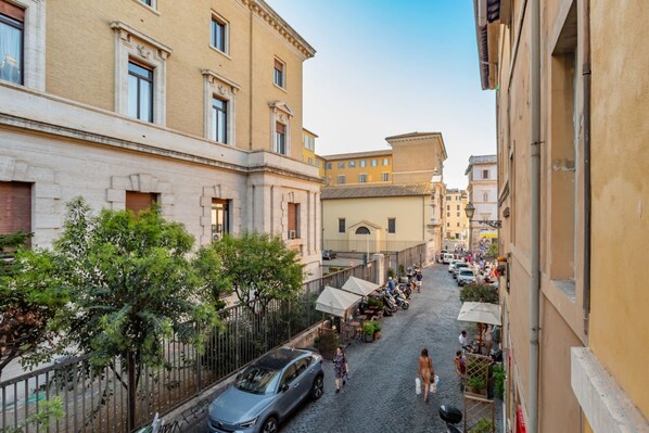 A cobblestone street lined with buildings, outdoor seating, and parked cars. - Daplace - Cosima Apartment (Roma)