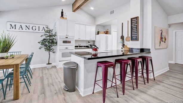 Une cuisine moderne avec des meubles blancs, une poutre en bois au plafond et un coin bar doté de tabourets rouges.