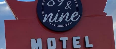 Een motelteken met de tekst '89 & negen' en 'MOTEL', een 'VACANTRY'-bord, en een Shell benzinestationbord.