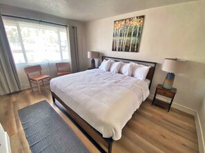 A neatly arranged bedroom with a large bed, two bedside tables with lamps, a chair, and a window with curtains. - 89 & Nine Motel (Orderville)