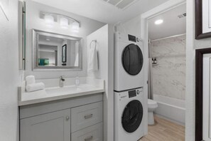 A modern bathroom with a built-in washer and dryer, a large mirror, and a marble-tiled shower area. - Modern, chic condo in the heart of Tempe/ASU
 (Tempe)