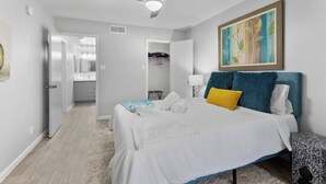 Une chambre à coucher avec un lit, un ventilateur de plafond, un tableau et une vue sur la cuisine.