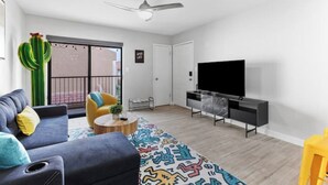 A modern living room with a grey sofa, a yellow armchair, a patterned rug, a flat-screen TV, and a ceiling fan. - Modern, stylish condo in Sun Devil Country
 (Tempe)
