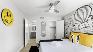 A bedroom with a bed, a ceiling fan, a wall with a smiley face artwork, and a wall with a hot air balloon and other doodles. - Modern, stylish condo in Sun Devil Country
 (Tempe)