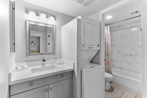 A modern bathroom with a white vanity, a mirror, a toilet, and a shower with a marble wall. - Modern, stylish condo in Sun Devil Country
(Tempe)