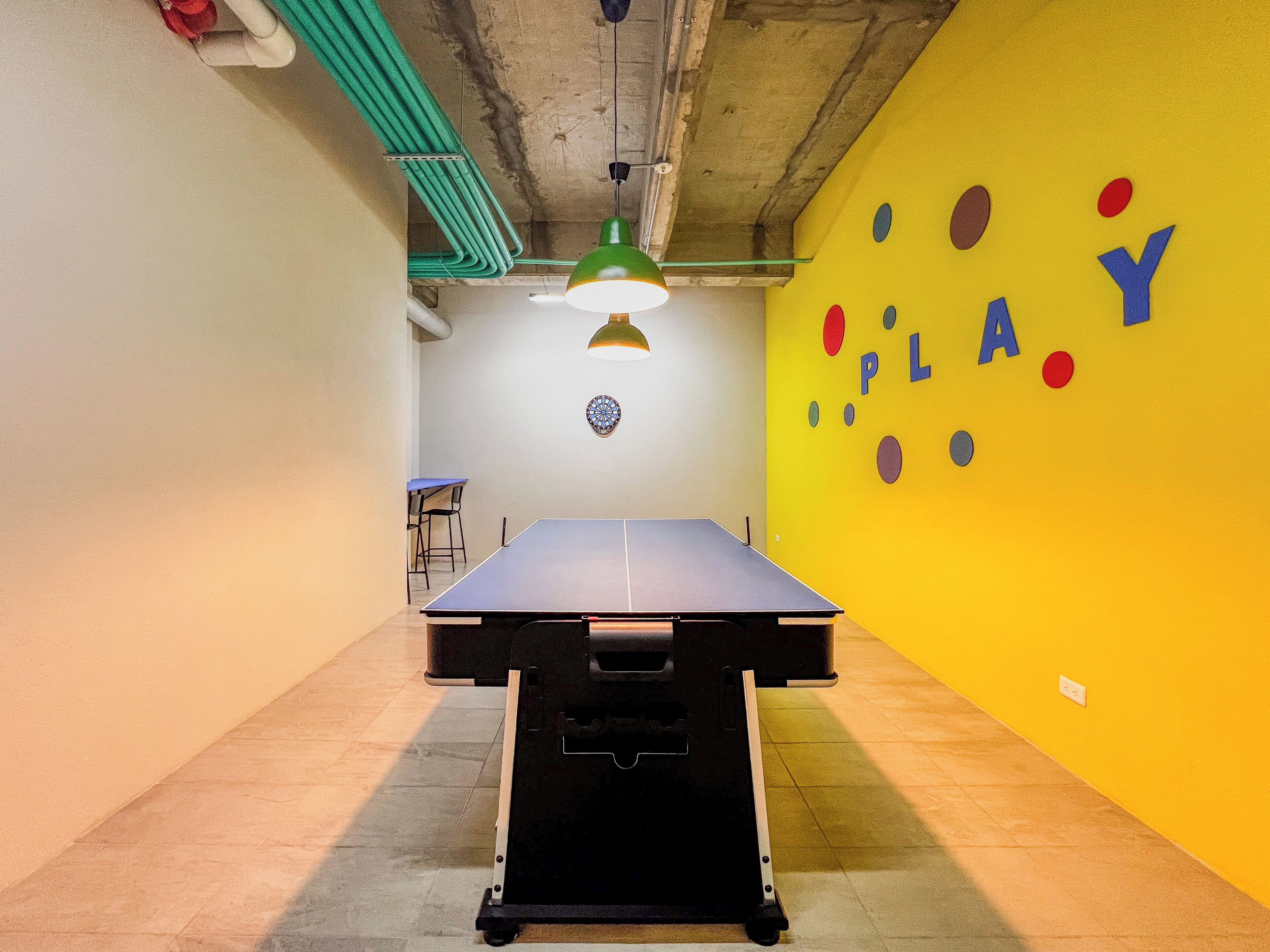 Une table de ping-pong dans une pièce avec un mur jaune et un jeu de fléchettes.