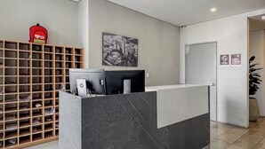 A reception desk with a black marble design, a wooden shelving unit with labeled compartments, and a large black and white artwork on the wall. - Nuevetres by Wynwood House (Bogotá)