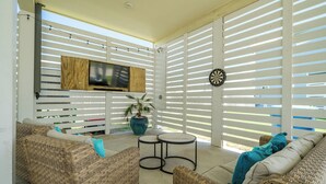 Un área de estar al aire libre techada con muebles de mimbre, un televisor de pantalla plana, un dardo y una planta en maceta.