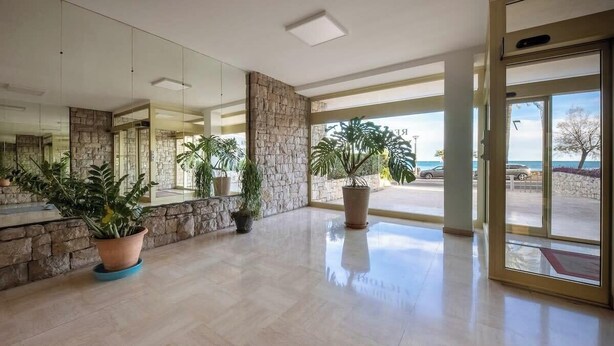 A spacious lobby with a stone wall, large potted plants, and a view of the outside. - 06B - Beautiful apartment with terrace sea view (Roquebrune-Cap-Martin)