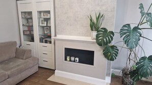 A living room with a beige sofa, a fireplace with a shelf, and a large potted plant. - Modern 4 bedroom house Dublin 20
 (Dublin)