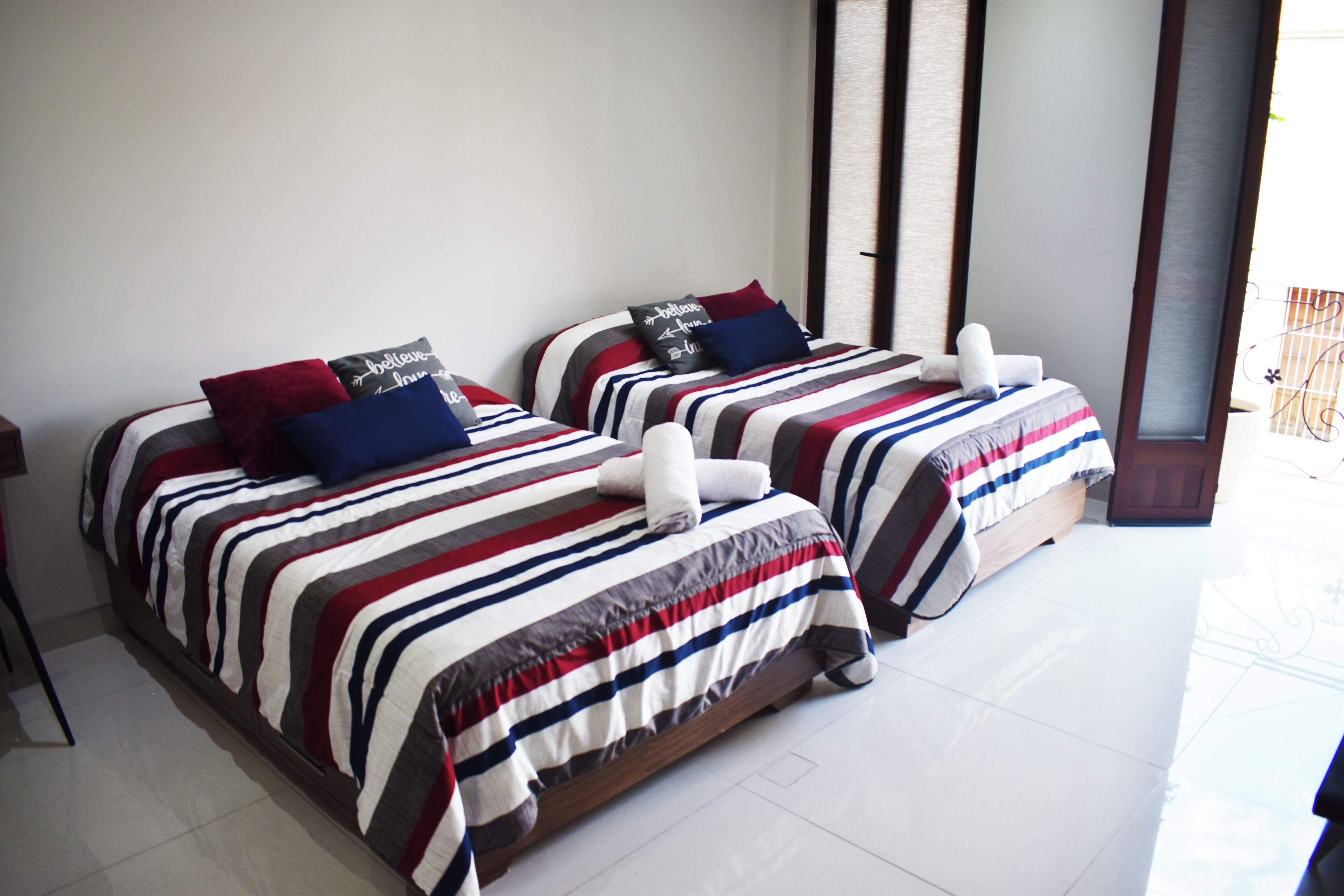 Two beds with striped bedding and pillows, a wooden headboard, and a white tiled floor.